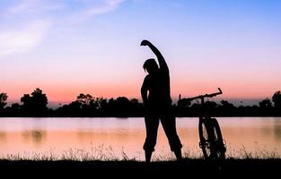 silueta mujer ejercicio cerca bicicleta en puesta de sol. foto