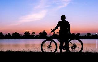 silueta mujer y bicicleta con lago en puesta de sol foto