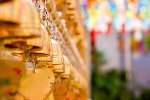 de cerca y perspectiva ver grupo de pequeño dorado campanas colgar en tailandés templo en borroso antecedentes. foto