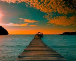 A wooden pier that stretches out to the sea,seascape view sunset with Mountain and cloudy sky for travel in holiday relax time as summer photo