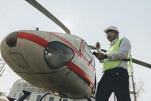 Asian man Aero Engineer Working On Helicopter In Hangar Looking At Digital Tablet photo