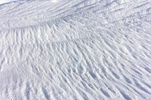 Abstract natural background of snow dunes and drifts. Strong wind makes bizarre snow patterns and textures on the surface of the field. A fancy natural pattern on a hard white snow cover. photo