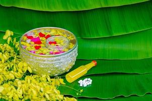 Songkran festival background with flowers in water bowls, scented water and marly limestone for blessing on wet banana leaf background.
