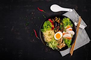 Japanese ramen soup with chicken, egg, shimeji mushrooms and eggplants on dark wooden background. Chanko nabe, sumo soup. Top view photo