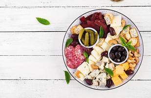 Antipasto platter with basturma, salami, blue cheese, nuts, pickles and olives on a white wooden background. Top view, overhead photo