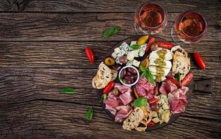 Antipasto platter with ham, prosciutto, salami, blue cheese, mozzarella with pesto and olives on a wooden background. Top view, overhead photo