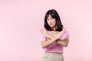 portrait serious young asian woman with cross arm gesture showing stop, no, wrong, denial, rejection sign isolated on pink pastel studio background. deny and negative expression symbol concept. photo