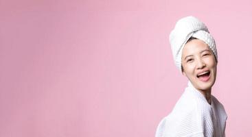 Beautiful young asian woman happy with clean face skin in towel and bathrobe, spa suit on pink background. Skincare, treatment, wellness therapy, facial care, beauty female health, cosmetology concept photo