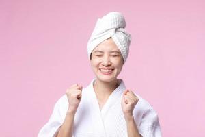 Beautiful young asian woman happy smile face with hand or finger gesture signs in bathrobe and shower towel showing empty space isolated on pink background.