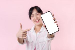 happy smiling young asian woman recommending showing new application or mobile advertisement, mockup smartphone template banner isolated on pink background. Collage blank screen digital mobile device. photo