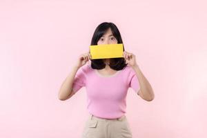 Portrait happy young woman model holding and showing blank space paper for advertisement information message poster with thumb up or point finger gesture isolated on pink pastel studio background. photo