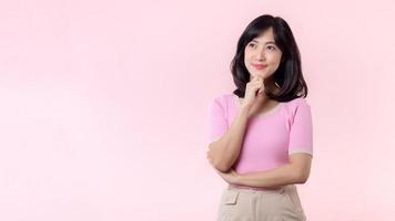 Portrait beautiful young asian woman thoughtful thinking an idea isolated on pink pastel background. Teenage female person pretty smile with thinking gesture concept. photo