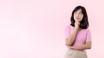 Portrait beautiful young asian woman thoughtful thinking an idea isolated on pink pastel background. Teenage female person pretty smile with thinking gesture concept. photo