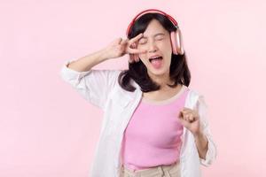 sonrisa bonito asiático modelo persona escucha música canción y disfrutar danza con inalámbrico auricular en línea audio radio sonido. positivo divertido salido alegre juventud hembra mujer en rosado aislado antecedentes estudio foto