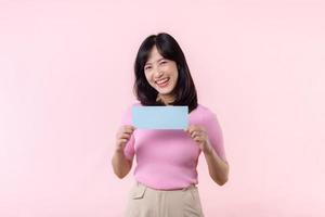 Portrait happy young woman model holding and showing blank space paper for advertisement information message poster with thumb up or point finger gesture isolated on pink pastel studio background. photo