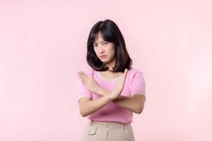 portrait serious young asian woman with cross arm gesture showing stop, no, wrong, denial, rejection sign isolated on pink pastel studio background. deny and negative expression symbol concept.
