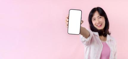 happy smiling young asian woman recommending showing new application or mobile advertisement, mockup smartphone template banner isolated on pink background. Collage blank screen digital mobile device.