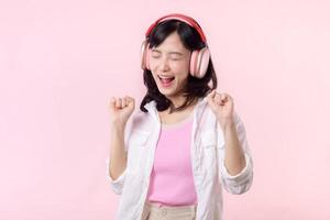 Smile pretty asian model person listen music song and enjoy dance with wireless headphone online audio radio sound. Positive fun exited joyful youth female woman on pink isolated background studio photo