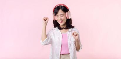 sonrisa bonito asiático modelo persona escucha música canción y disfrutar danza con inalámbrico auricular en línea audio radio sonido. positivo divertido salido alegre juventud hembra mujer en rosado aislado antecedentes estudio