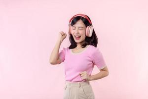 Smile pretty model person listen music song and enjoy dance with wireless headphone online audio radio sound. Positive fun exited joyful youth female woman sing on pink isolated background studio photo