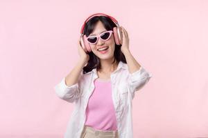 contento joven asiático mujer modelo con elegante de moda Dom lentes disfrutar escuchando música por auricular audio y bailando aislado en rosado estudio antecedentes. tecnología, niña moda, accesorio concepto. foto