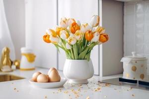 Easter table setting with tulips, Easter bunnies, and eggs with golden patterns in the white Scandinavian-style kitchen background. Beautiful minimalist design for greeting card photo
