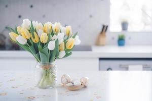 Pascua de Resurrección mesa ajuste con tulipanes, Pascua de Resurrección conejitos, y huevos con dorado patrones en el blanco estilo escandinavo cocina antecedentes. hermosa minimalista diseño para saludo tarjeta foto