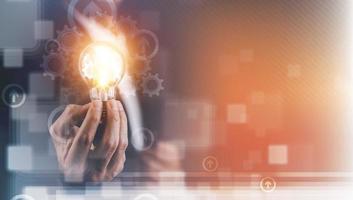 Businessman hand holding light bulb with icons and working on the desk, Creativity and innovation are keys to success.Concept of new idea and innovation with energy and power , working at home, photo