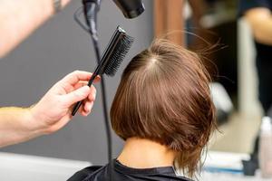 Hairdresser dries brown hair of woman photo