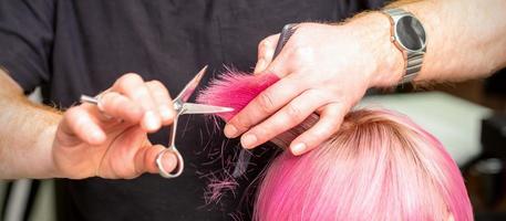 Hairdresser cutting short pink hair photo