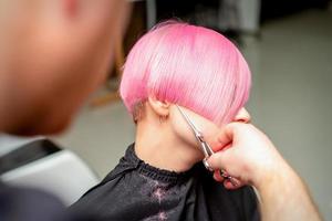 Hairdresser cutting short pink hair photo