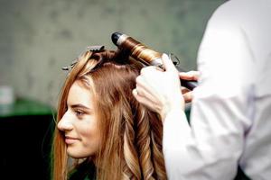 Hairdresser makes curls with curling iron photo