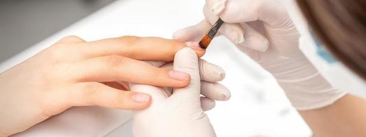 Manicurist covering nails with transparent polish photo