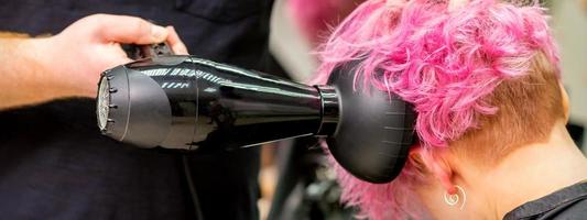Hairdresser drying short pink hair photo