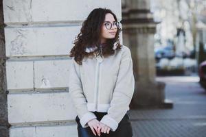 Beautiful young woman with brunette curly hair, portrait in eye glasses enjoying the sun in the city. photo