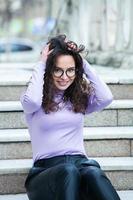 hermosa joven mujer con morena Rizado cabello, retrato en ojo lentes disfrutando el Dom en el ciudad. foto