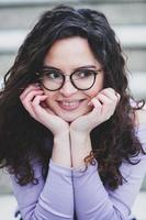 Beautiful young woman with brunette curly hair, portrait in eye glasses enjoying the sun in the city. photo