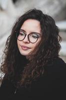 Beautiful young woman with brunette curly hair, portrait in eye glasses enjoying the sun in the city. photo