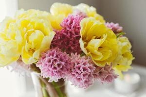 Beautiful yellow peony tulips and pink hyacinth flower bouquet on white dresser. photo