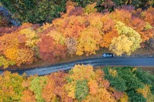 Aerial view of a car standing on the side of the road surrounded by autumn colored trees photo