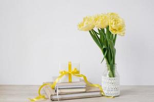 A lot of notepads in a stack, a bouquet of yellow spring tulips and a gift box on the desktop of a freelancer or blogger woman. Women's day, valentine's day or birthday. Front views photo