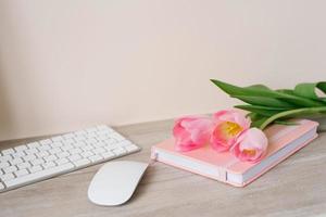 Workspace with keyboard, pink diary and pink tulips on wooden background. Space for text photo