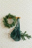 Christmas decor in the living room in the Scandinavian style, a wreath of fir branches on the wall and a rag mesh bag string bag hanging on a hook photo
