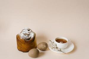 An Easter composition with a cake and eggs and a cup of tea with a sprig of a flowering apple tree on a light background. Easter vacation breakfast concept with copy space. photo