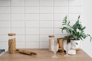 A glass jar with pasta, glasses, a rolling pin and a houseplant stand in the bright kitchen. Kitchen utensils, Scandinavian style photo