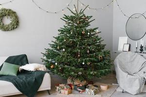 A beautiful Christmas tree fir with toys and a sofa with pillows in the interior of the living room in the Scandinavian style with gray walls photo