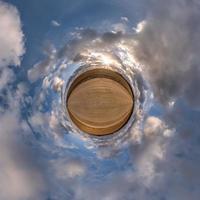 tiny planet in blue overcast evening sky with beautiful clouds with transformation of spherical panorama 360 degrees. Spherical abstract aerial view. Curvature of space. photo