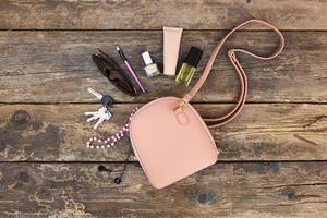 cosas desde abierto dama cartera. productos cosméticos y De las mujeres accesorios cayó fuera de bolso en antiguo de madera antecedentes. parte superior vista. foto