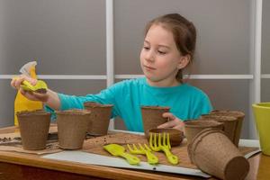 pretty girl at the table pours earth into peat pots, prepares for planting seedlings photo