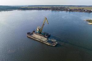 aerial view on crane extracts minerals from bottom onto huge barge in middle of lake or sea photo